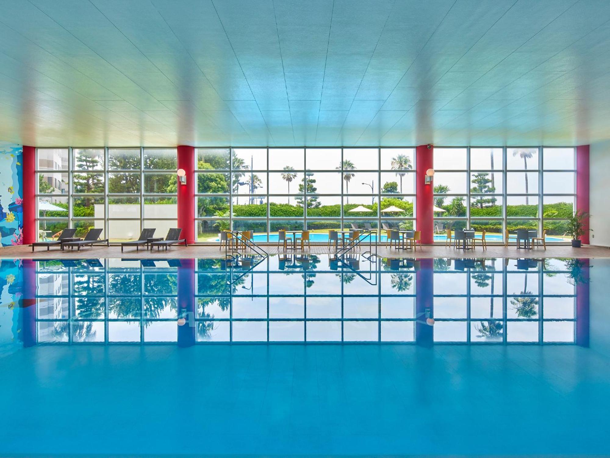 فندق Grand Nikko Tokyo Bay Maihama Urayasu المظهر الخارجي الصورة The photo shows an indoor swimming pool with bright blue water. The pool area is spacious, characterized by large windows that allow natural light to flood in, creating a vibrant atmosphere. The walls are painted in a soft color, with accents of red.