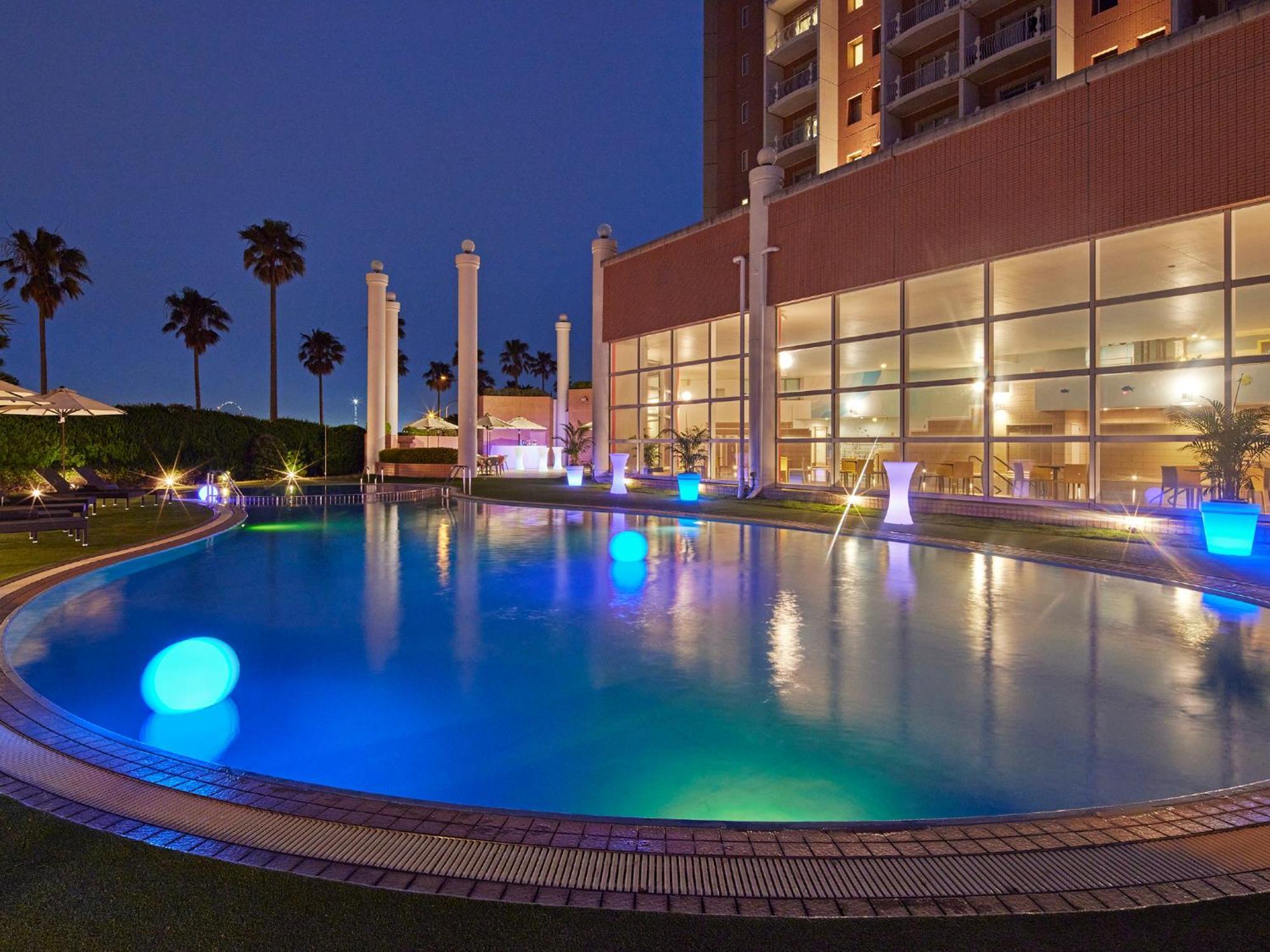فندق Grand Nikko Tokyo Bay Maihama Urayasu المظهر الخارجي الصورة The photo shows a well-lit swimming pool at night, surrounded by a lush green area. The pool features glowing blue lights that create a serene and inviting atmosphere. Palm trees can be seen in the background, adding a tropical feel to the scene. Add